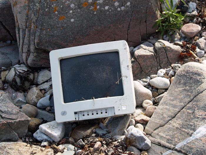A discarded computer monitor sitting amid a pile of rocks.